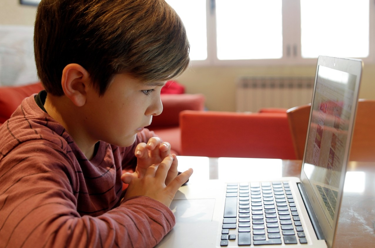 Un niño estudia en casa con un portátil. 